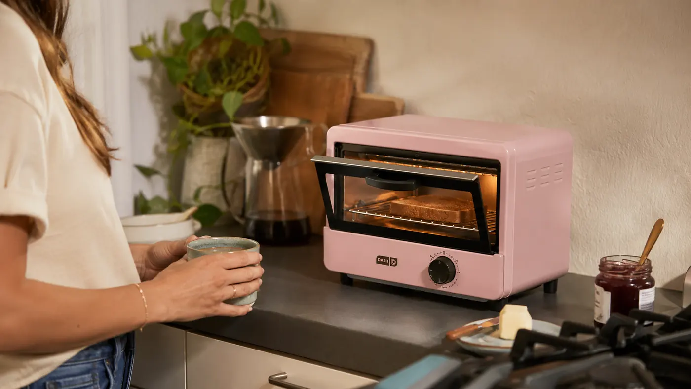 Dash Mini Toaster Oven sitting on a narrow apartment counter with toast visible inside through the door