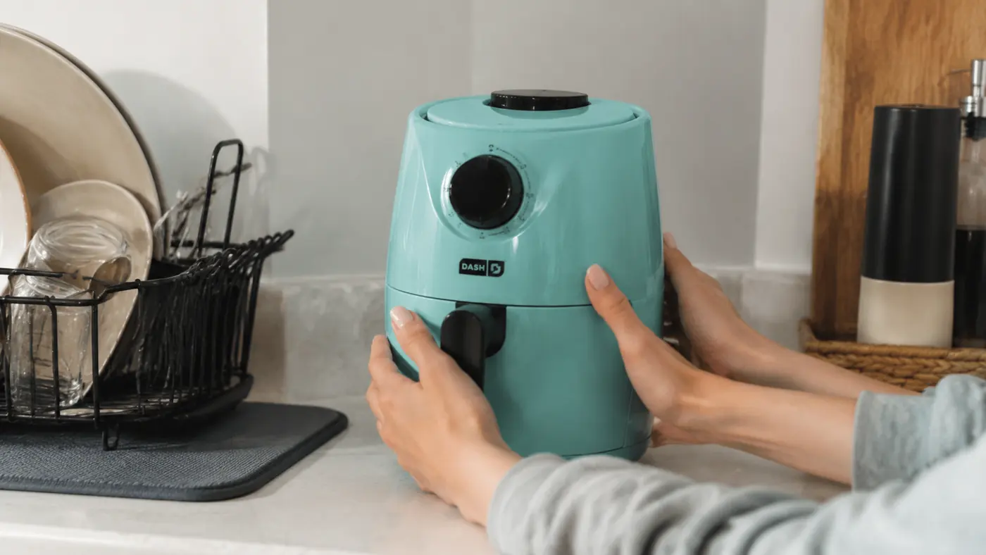 Hand setting the Dash Tasti-Crisp air fryer down on a cleared three-foot counter next to the stove