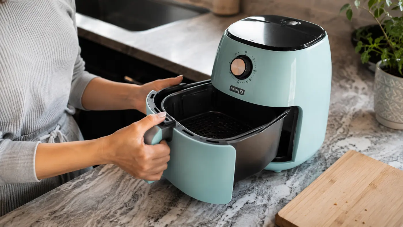 Hand pulling open the DASH air fryer basket to show the actual usable cooking space inside