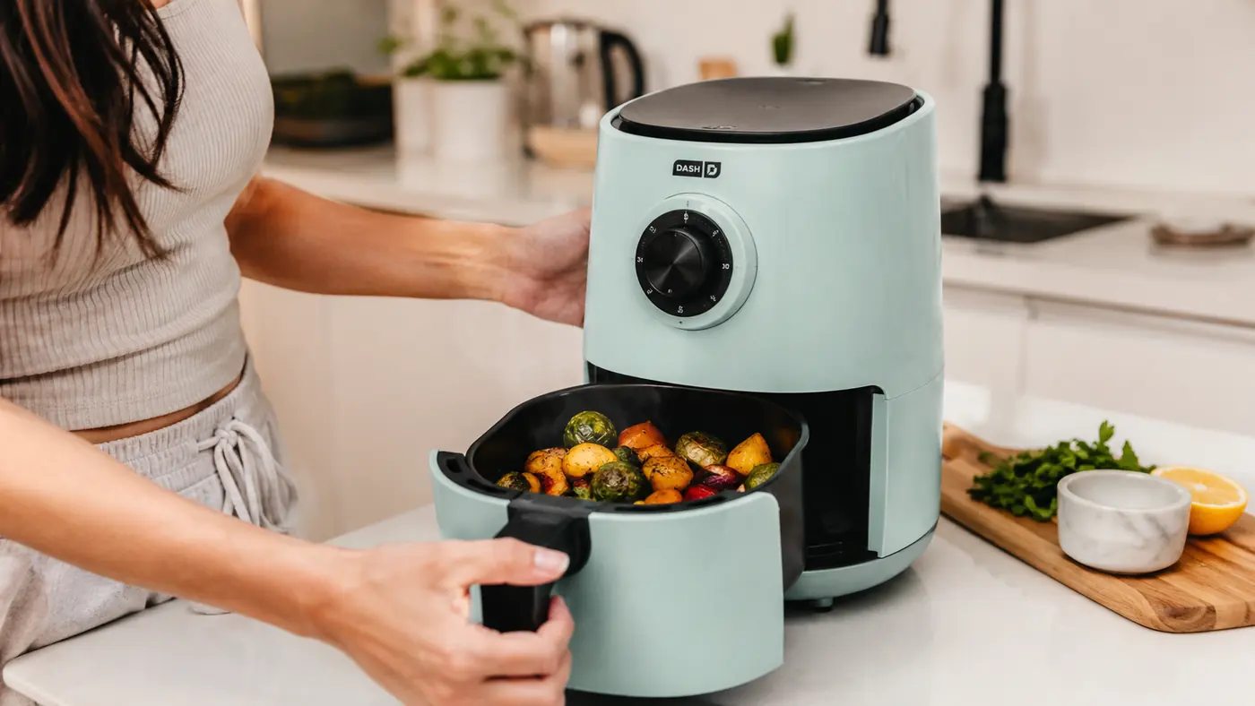 Hand pulling out the basket of the Dash Tasti-Crisp air fryer to check on roasted vegetables