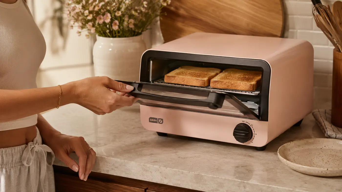 Hand opening the door of the DASH Mini Toaster Oven to check on toasted bread inside