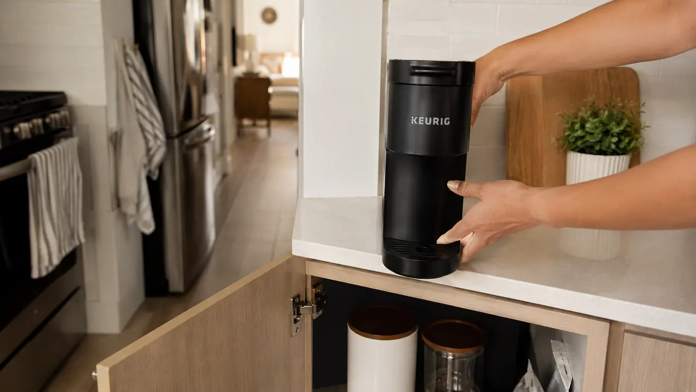 Hand plugging in the Keurig K-Mini Mate on a cleared strip of counter next to the stove