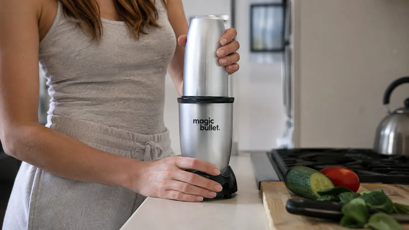 Hand twisting the Magic Bullet blending cup onto the base on a tight strip of counter next to the sink